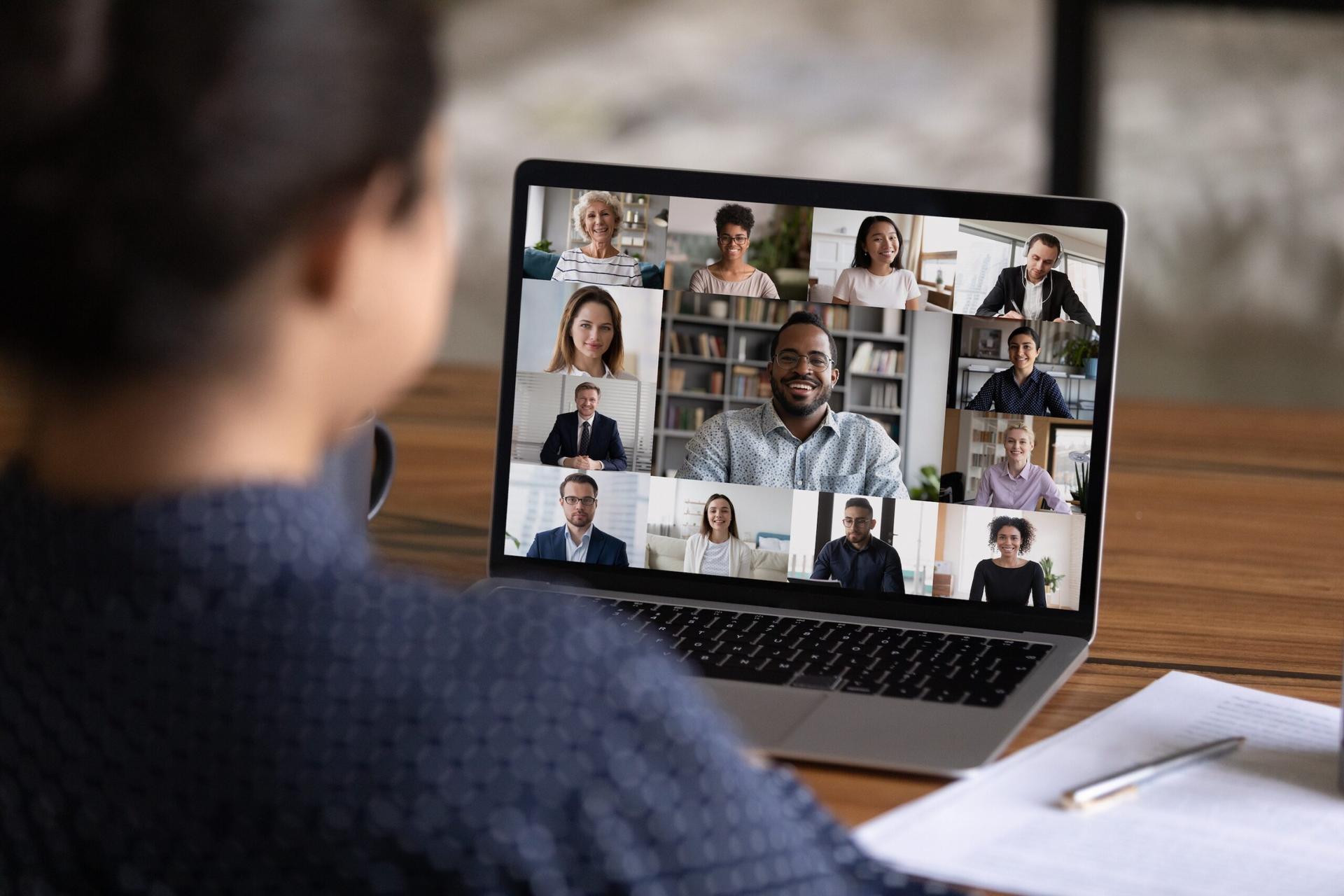 Blurred back of a person in from of a tablet filled with faces of people on a videoconferencing platform